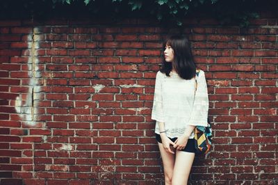 Beautiful woman looking away while standing against brick wall