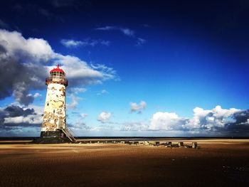 Lighthouse on beach against cloudy sky