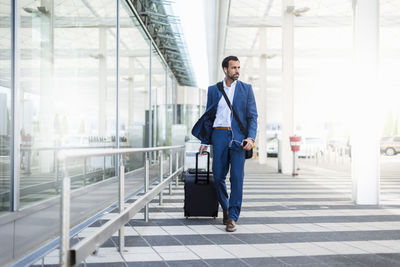 Businessman with trolley and smartphone at airport