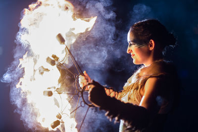 Side view of young woman with arms outstretched at night