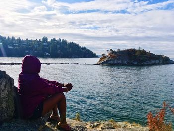 Rear view of woman sitting on rock against sky