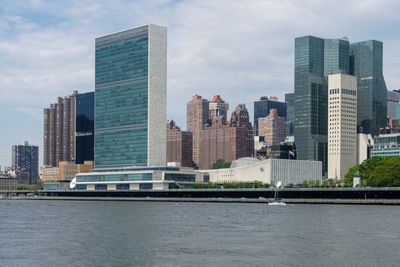 Modern buildings by river against sky in city