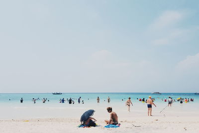 People at beach against cloudy sky on sunny day