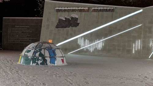 Rear view of person on illuminated footpath against building at night