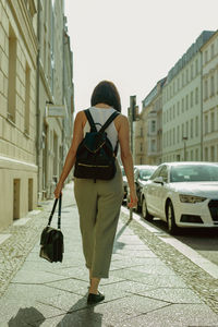 Rear view of woman walking on sidewalk in city during sunny day