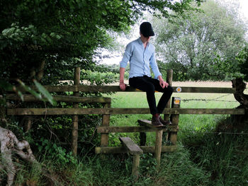 Full length of man sitting on wooden fence