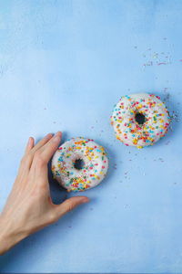 Cropped hand of person reaching for donut on blue background