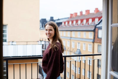 Side view of smiling woman standing in balcony at rental apartment