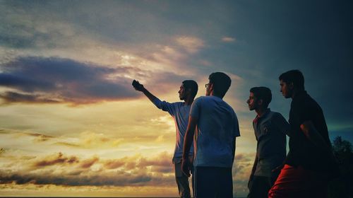 Friends taking selfie through mobile phone against sky