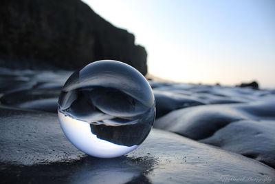 Close-up of crystal ball on rock at beach against sky