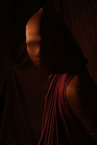 Close-up portrait of woman wearing mask while standing against black background
