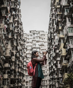 Low angle view of woman photographing while standing against buildings in city