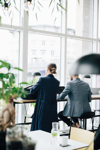 Rear view of businesswoman with bag by male colleague in cafeteria at office