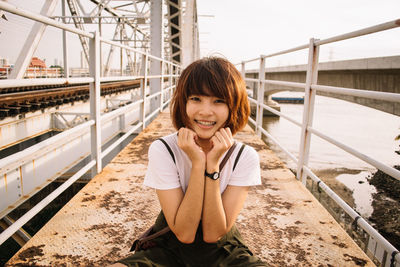 Portrait of smiling woman sitting on railing