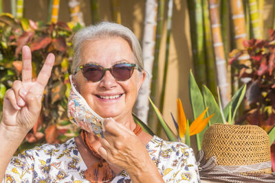 Portrait of smiling senior woman wearing mask gesturing against plants