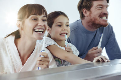 Family of three brushing their teeth in front of big mirror