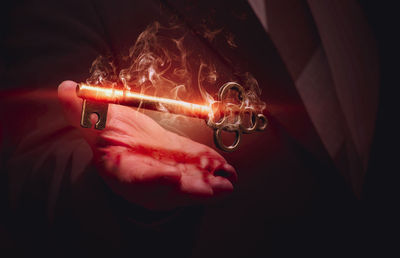 Close-up of hand holding lit candle against black background