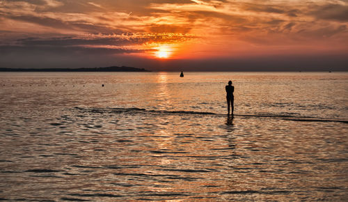 Silhouette person standing on beach against sky during sunset