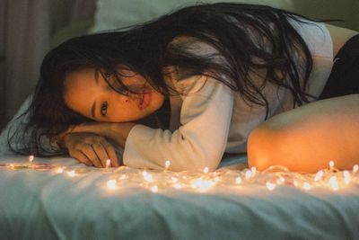 Portrait of beautiful woman relaxing by illuminated lights on bed at home