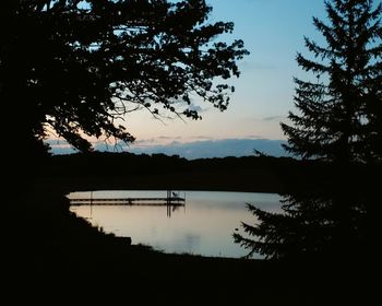 Silhouette trees by lake against sky during sunset