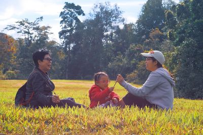 Boys sitting on field against trees