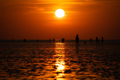 Silhouette people on sea against orange sky