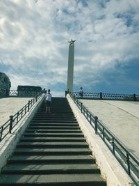 People on staircase by bridge against sky