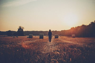 Rear view of woman on agricultural field against sky during sunset