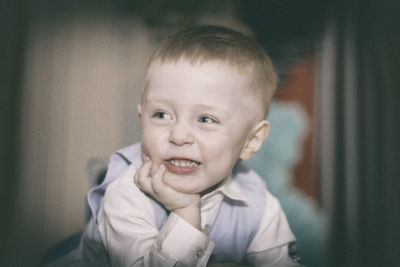 Close-up of smiling boy with hand on chin at home