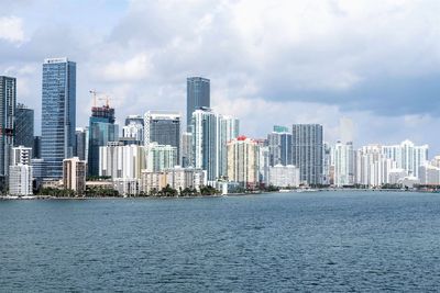 Sea by modern buildings against sky in city