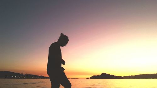 Silhouette man standing on beach against clear sky during sunset