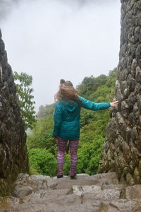 Rear view of woman standing on rock against sky