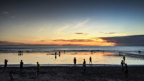 Silhouette people standing on beach against sky during sunset