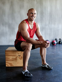 Smiling male athlete sitting on wooden box in gym