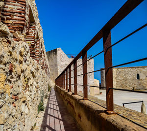 Footpath by wall against clear blue sky