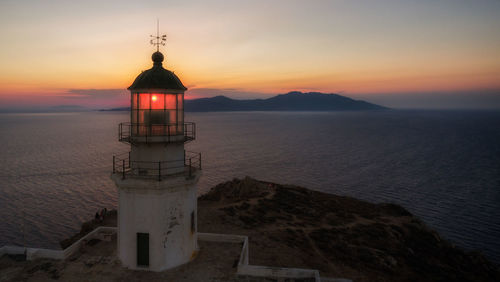 Lighthouse by sea against sky during sunset