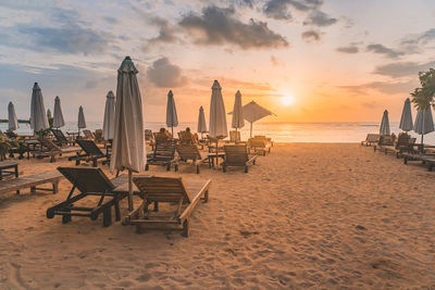 Chairs on beach against sky during sunset