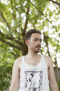 Portrait of young man looking away against trees