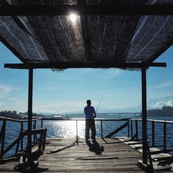 Rear view of man standing on railing against sea