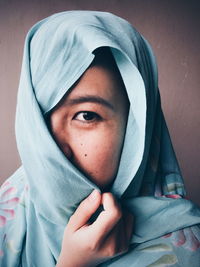 Close-up portrait of woman wearing hijab against wall