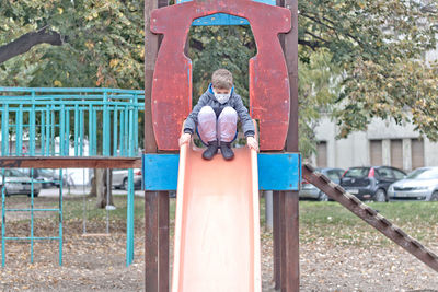 Little boy wearing face mask while sliding in the park.