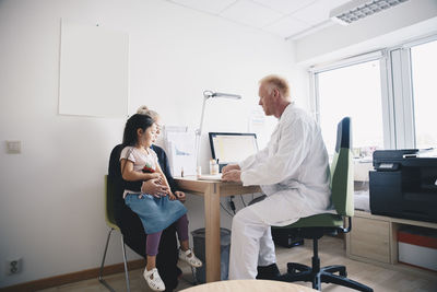 Mature doctor sitting with woman and girl in office at hospital