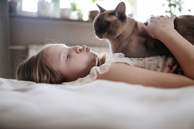 Side view of cute girl playing with cat at home