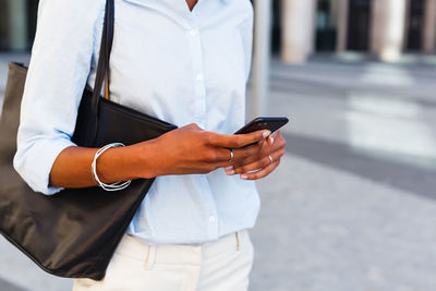 Midsection of woman using mobile phone in city