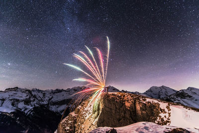 Firework display over mountains against clear sky at night