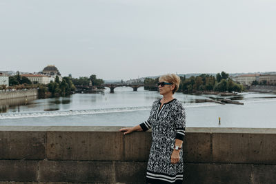 An elderly woman stands on the charles bridge on a summer day.