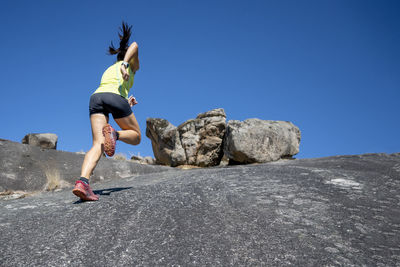 Female athlete running up on rock mountain during sunny day