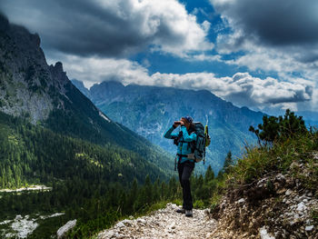 Full length of woman looking through binoculars while standing on mountains against sky