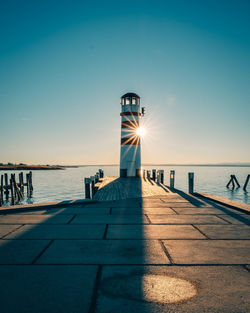 Lighthouse by sea against clear blue sky