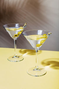 Two glasses of martini cocktails with green olives, on background of shadow of tropical plants